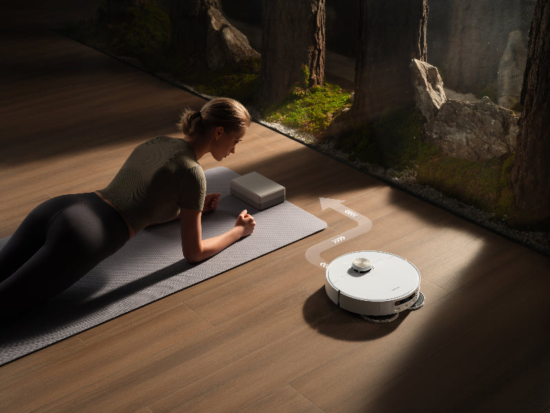 a woman doing plank on a mat next to a robot vacuum cleaner